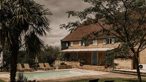 Una casa in pietra con piscina, area salotto esterna e vegetazione rigogliosa.