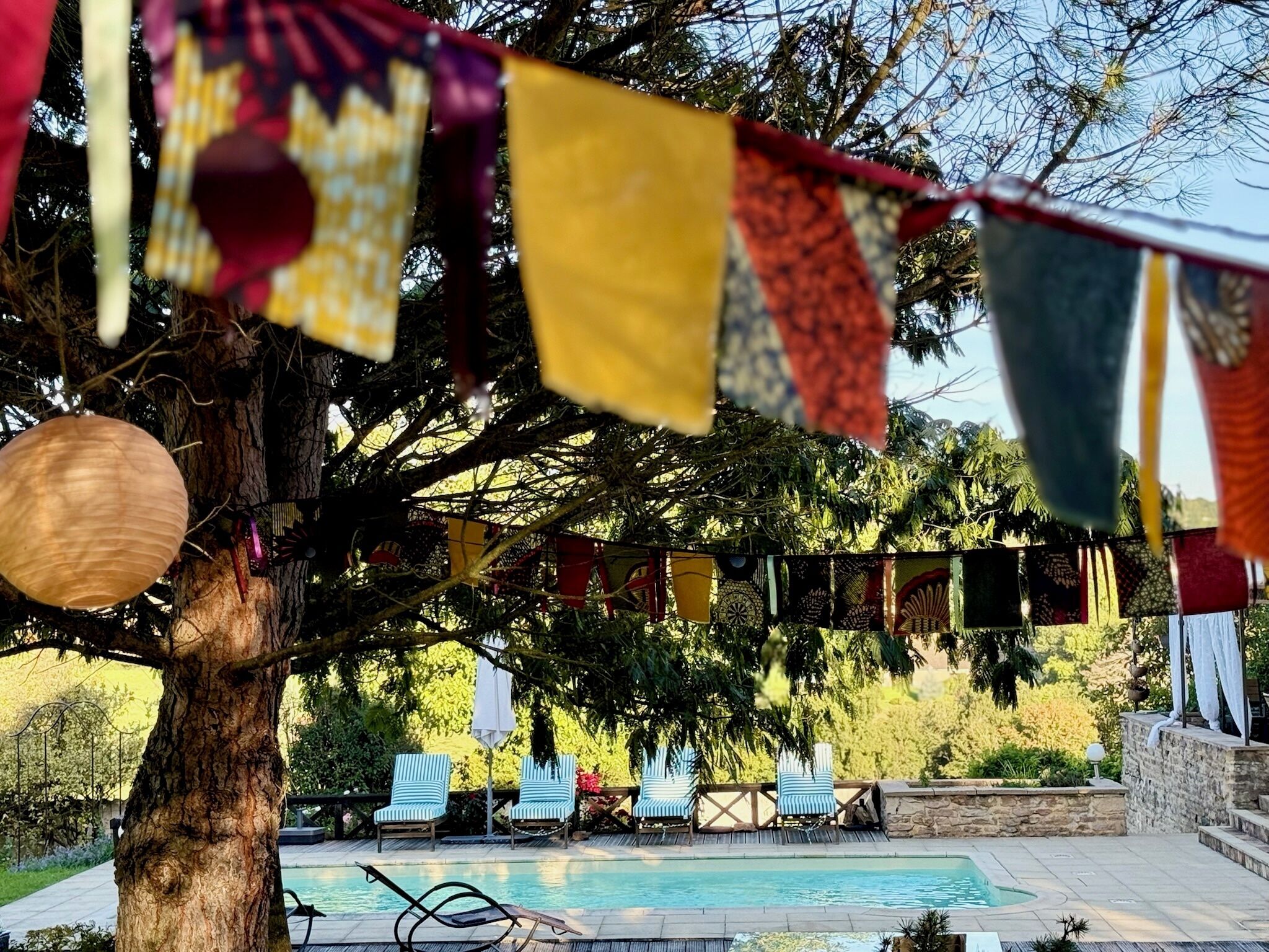Zona junto a la piscina con sillones, un árbol y una guirnalda de banderas de colores.