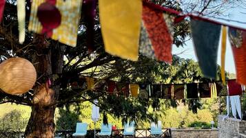 Zona junto a la piscina con sillones, un árbol y una guirnalda de banderas de colores.