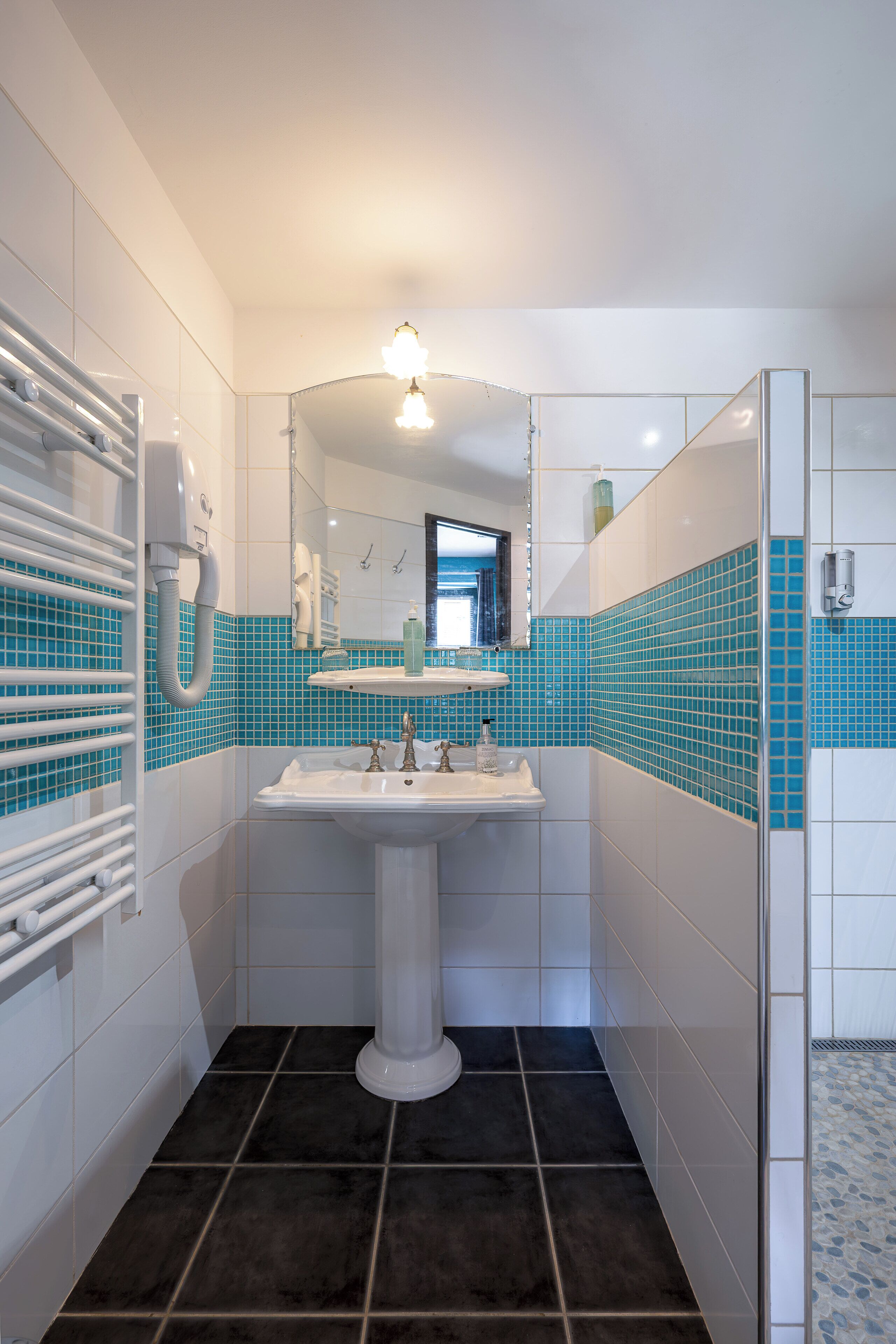 A bathroom with a white sink, a mirror, a towel rack, and a shower area.