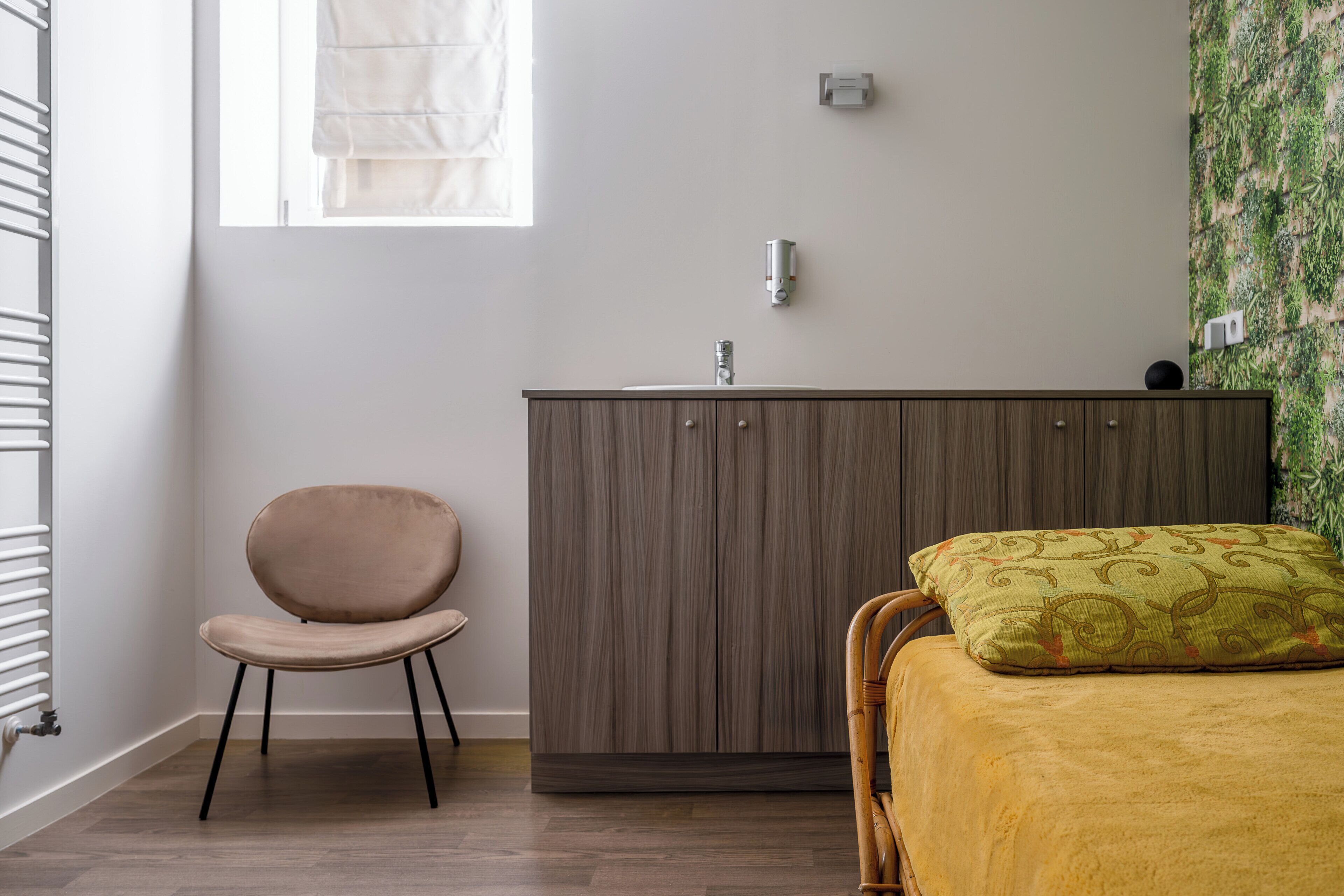 Een slaapkamer met een bed, een houten garderobe, een stoel, een radiator en een raam.