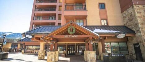 A hotel entrance with a wooden facade, a sign reading "SHAVANO," and a mountain backdrop.