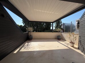 A covered outdoor area with a concrete floor, two potted plants, and a view of trees and buildings in the background. - Loft near downtown (Nevers)
