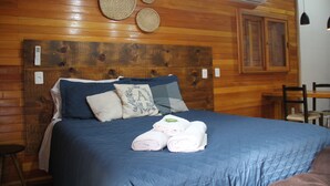 Un lit bien fait, avec une literie bleue et des serviettes enroulées, une tête de lit en bois et un climatiseur fixé au mur.