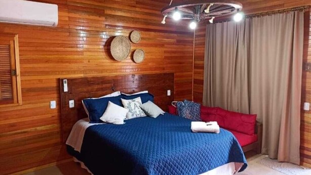 Une chambre aux murs lambrissés, avec un lit, un canapé rouge et un ventilateur de plafond.