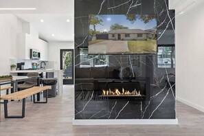 A modern living room with a fireplace, a dining area, and a kitchen.