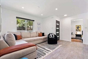 A modern living room with a sofa, a black armchair, a rug, and a door leading to another room.