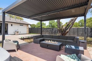 An outdoor patio with a sectional sofa, a fire pit, and a covered seating area.