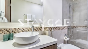 Ein modernes Badezimmer mit einem großen, weißen Waschbecken, einer Duschkabine aus Glas und einem gefliesten Duschbereich.