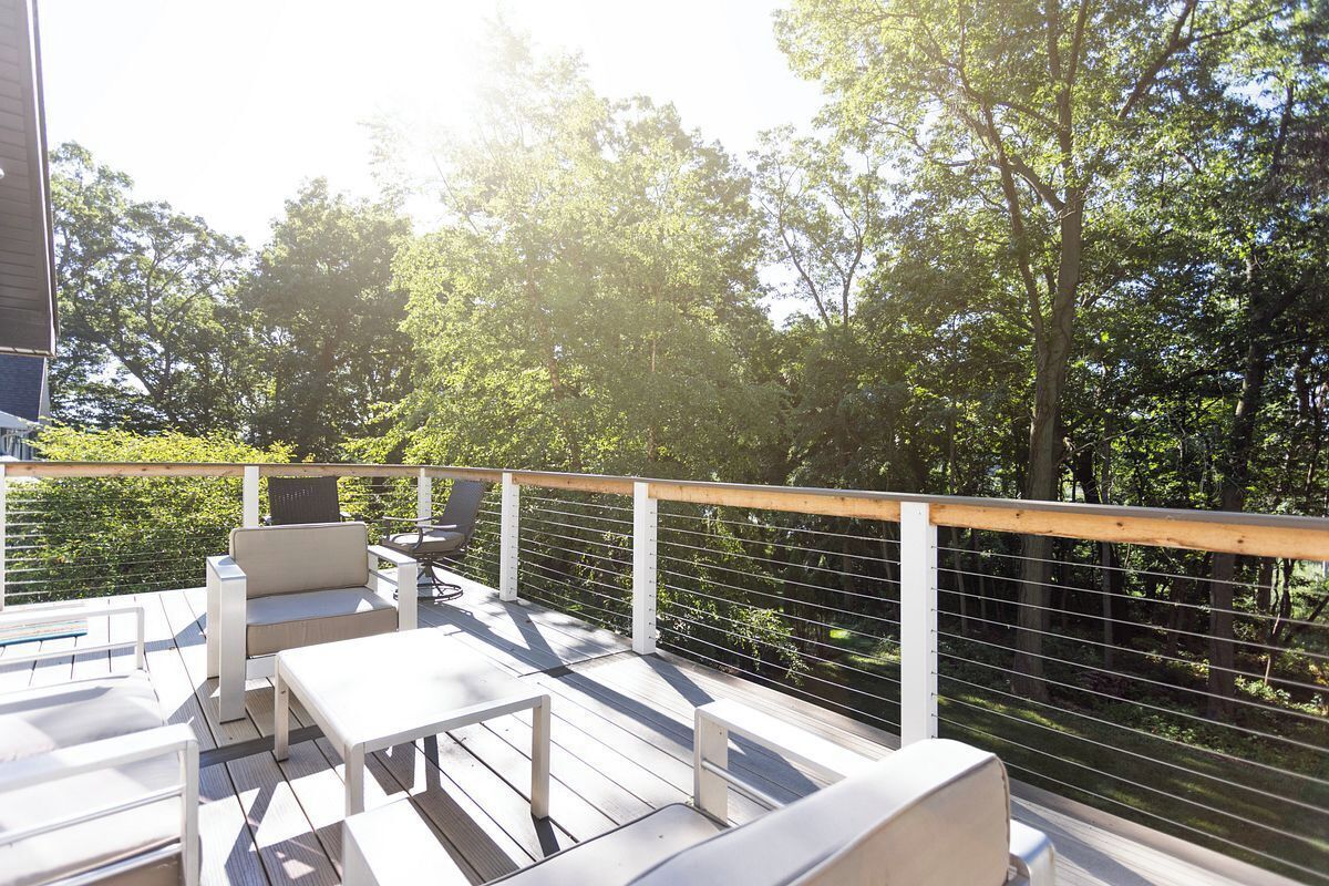 An outdoor deck with white furniture, including a sofa and a table, surrounded by a wooden railing.