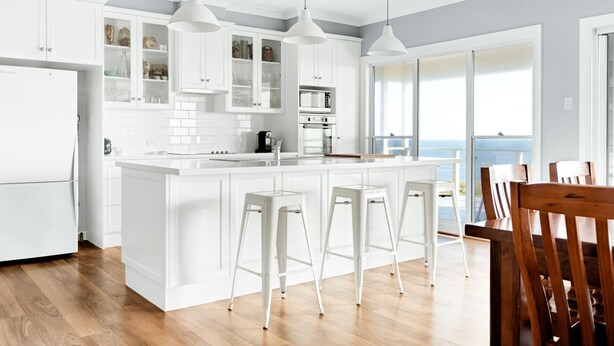 A modern kitchen with white cabinetry, a central island with bar stools, and a view of the ocean through large windows.