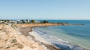 A coastal area with a sandy beach, clear blue sea, and a row of houses along the shore.