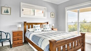 A bedroom with a wooden bed, two nightstands, a chair, and a large window with a view of the outdoors.