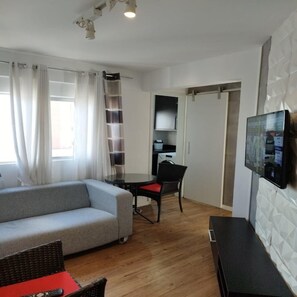 A modern living room with a grey sofa, a black TV on the wall, a wooden floor, and a dining area with a table and chairs. - Apartamento Charles Chapelin  (Curitiba)
