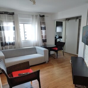 A modern living room with a sofa, a dining table, and a TV. - Apartamento Charles Chapelin  (Curitiba)