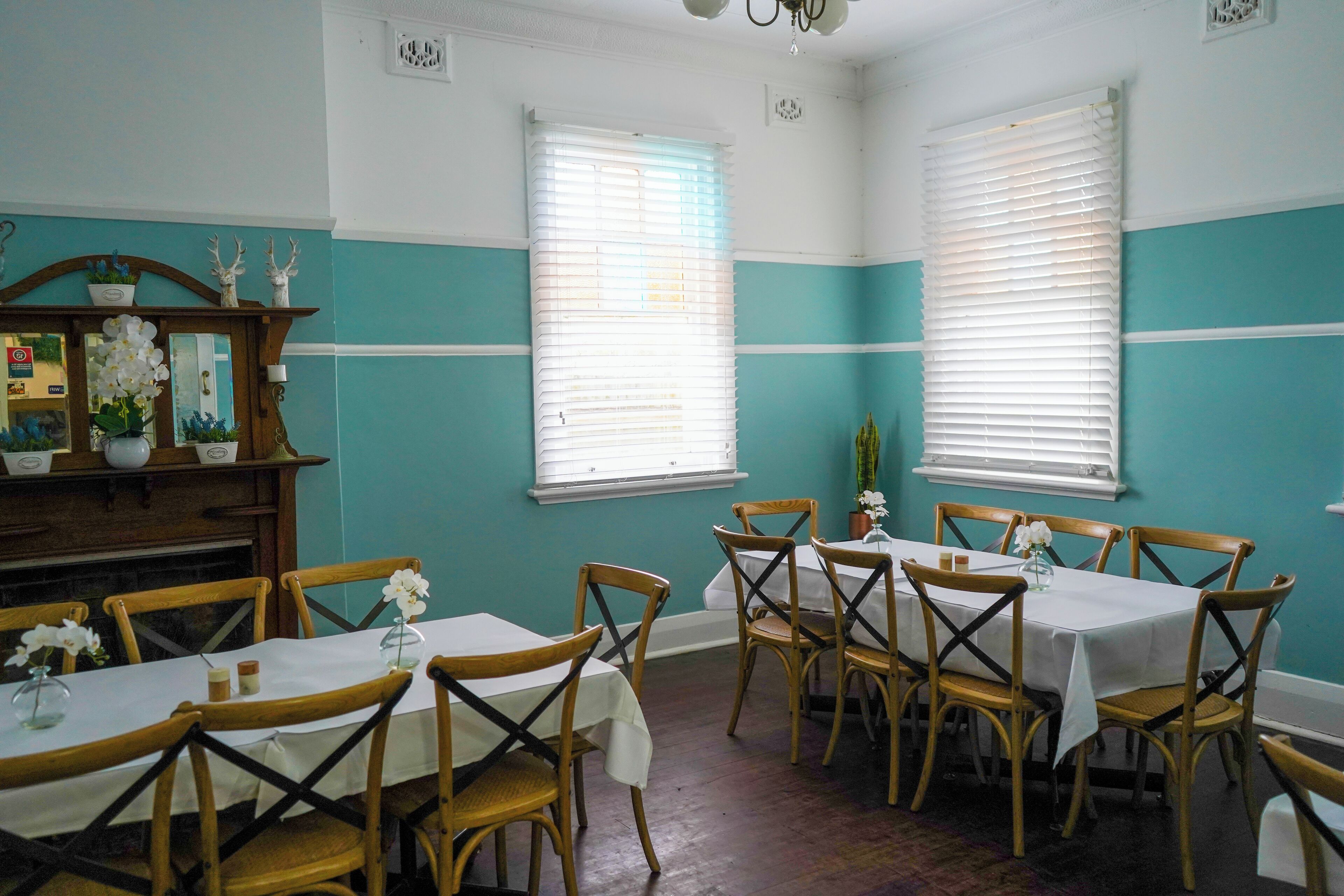 A dining area with wooden tables and chairs, teal walls, and white trim.