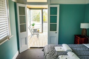 A bedroom with a bed, a nightstand, a chair, a small table with a plant, and a door leading to a balcony. - Khartoum Hotel (Kitchener)