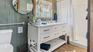 A bathroom with a white vanity, a round mirror, a toilet, and a shower area. - Lucky Star Ranch - Stargazer (Bandera)