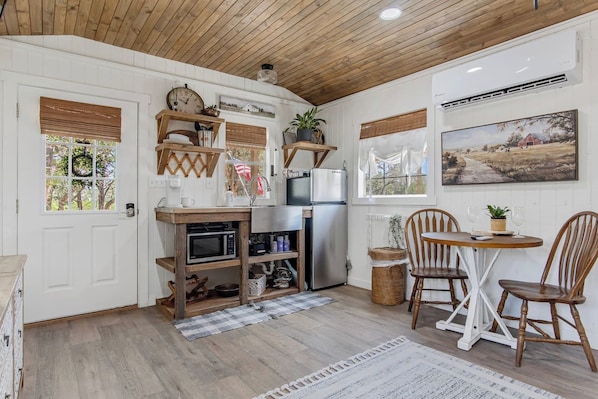 A compact kitchen with a wooden ceiling, white walls, a refrigerator, a microwave, and a dining area with two chairs and a table. - Lucky Shooting Star #3 | Romantic Stay Near Parks (Bandera)