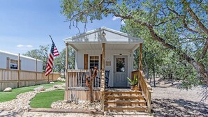 A small, single-story building with a porch, a flag, and a mailbox. - Lucky Star Ranch - Shooting Star (Bandera)