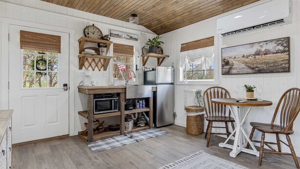A kitchen with wooden cabinets, a refrigerator, a microwave, and a dining area with two wooden chairs and a small table. - Lucky Star Ranch - Shooting Star (Bandera)