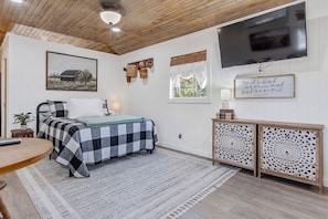 Quarto com cama, mesa de cabeceira, luminária, TV e objetos decorativos.