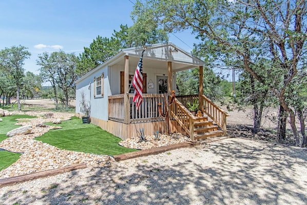 A small house with a porch, a flag, and a well-maintained lawn.