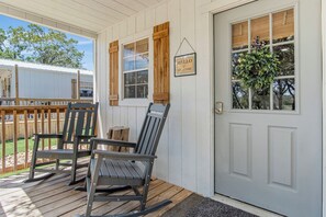 A porch with two rocking chairs, a wooden deck, and a white door with a welcome sign. - Lucky Shooting Star #3 | Romantic Stay Near Parks (Bandera)
