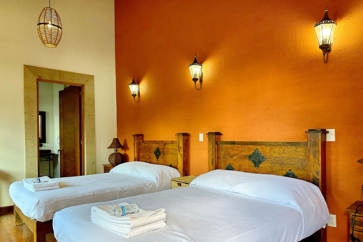 A hotel room with two beds, wooden headboards, and wall-mounted lamps.