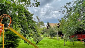 A playground with a yellow slide and a swing set in a grassy yard with trees and a house in the background. - Sandunga Suites Patzcuaro (Patzcuaro)