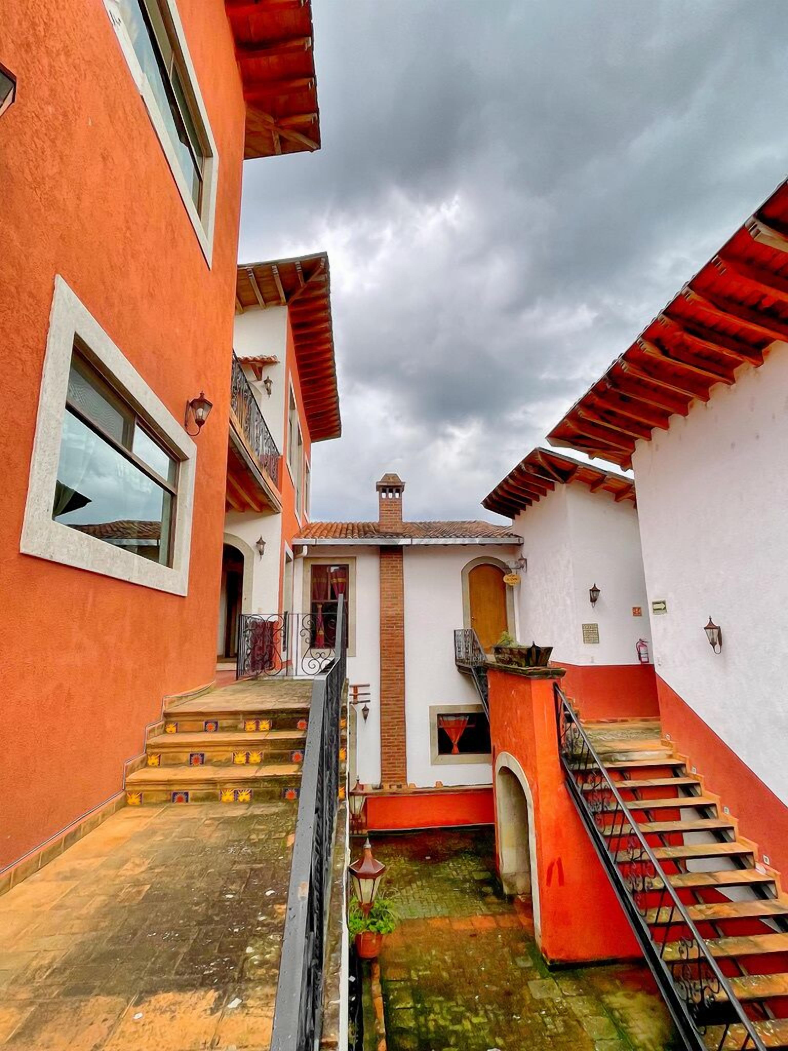 A narrow alleyway between buildings with red and white facades, a small staircase, and a tiled ground.