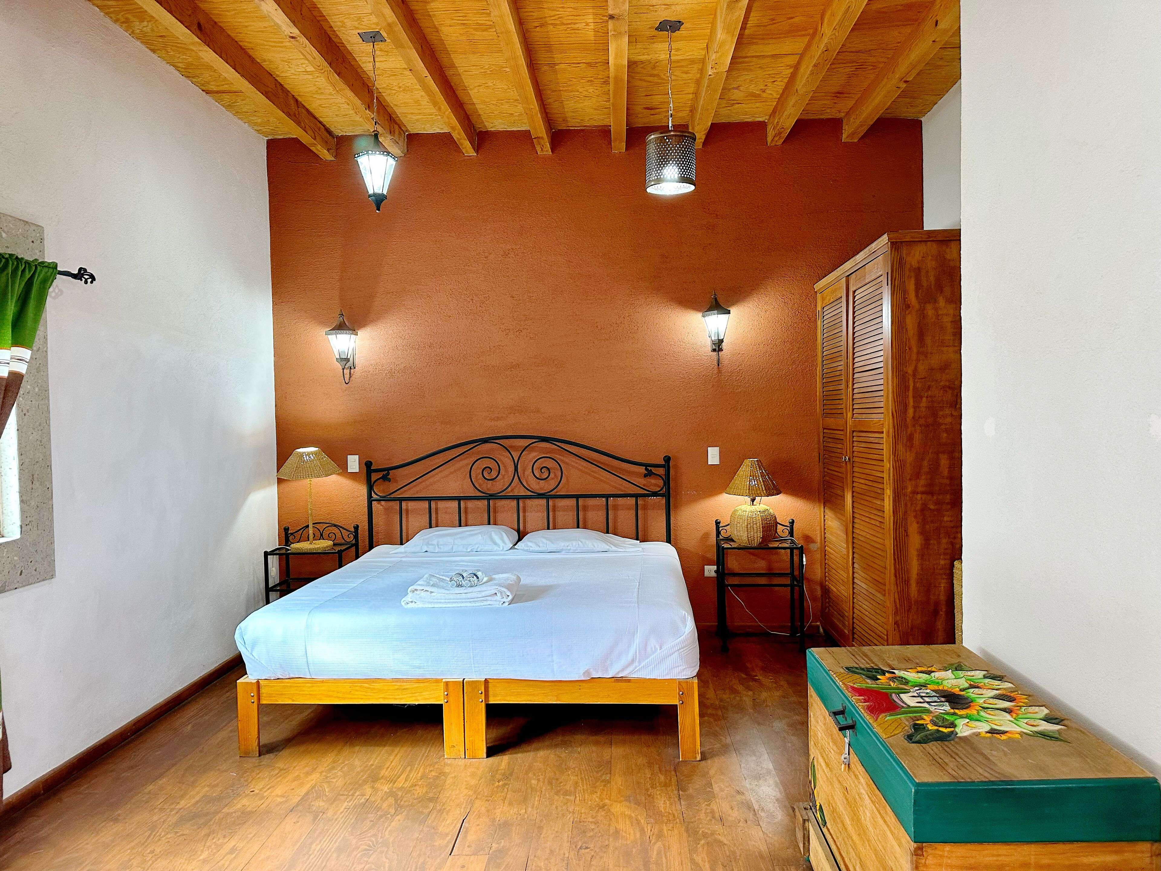 Ein Schlafzimmer mit einem hölzernen Bett, zwei Nachttischen mit Lampen, einem Holzschrank und einer grünen Kommode.