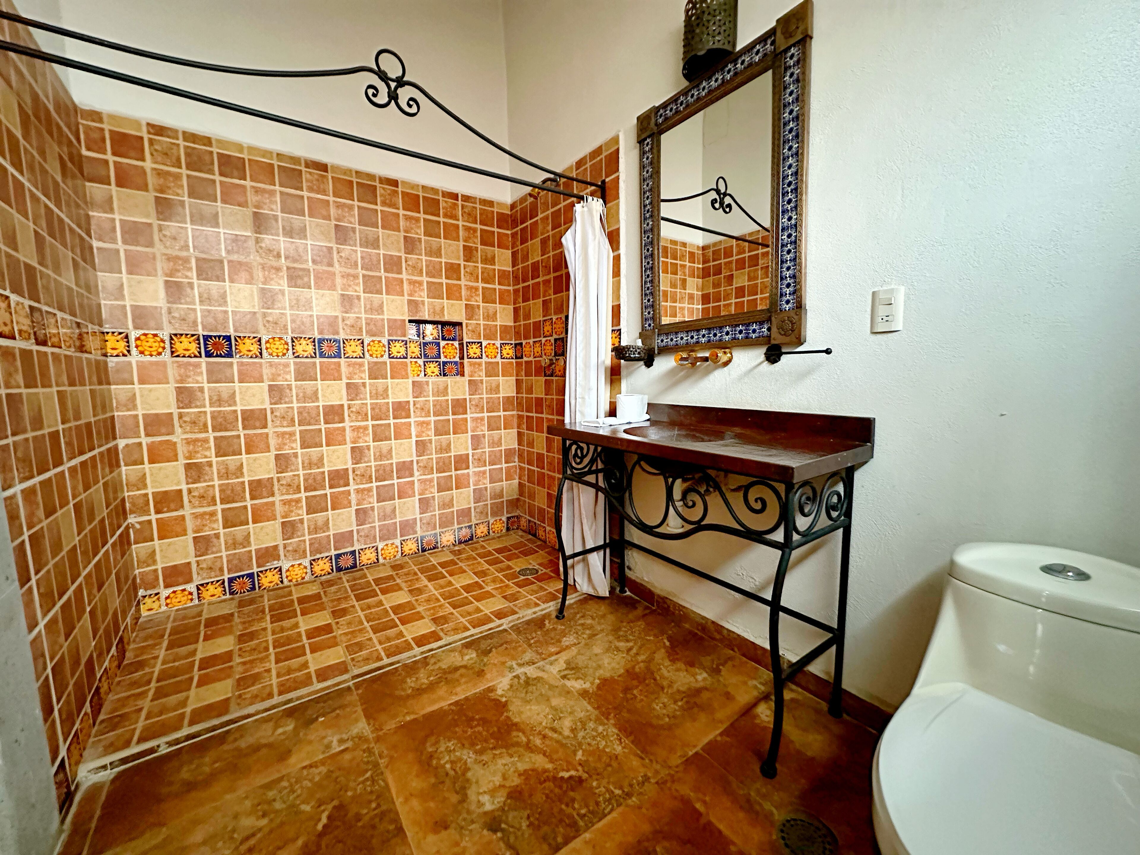 A bathroom with a tiled shower area, a sink with a mirror, and a toilet.