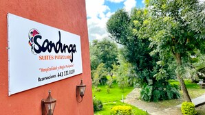 A sign for 'Sardonga Suites Pátzcuaro' with a contact number and a view of a lush garden. - Sandunga Suites Patzcuaro (Patzcuaro)
