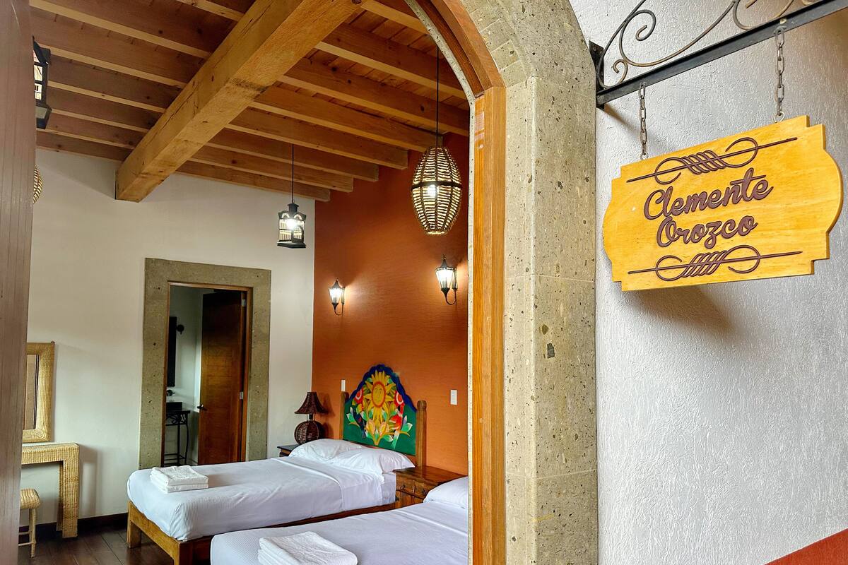 A hotel room with two beds, wooden beams on the ceiling, a wall-mounted sign, and a decorative wall hanging.