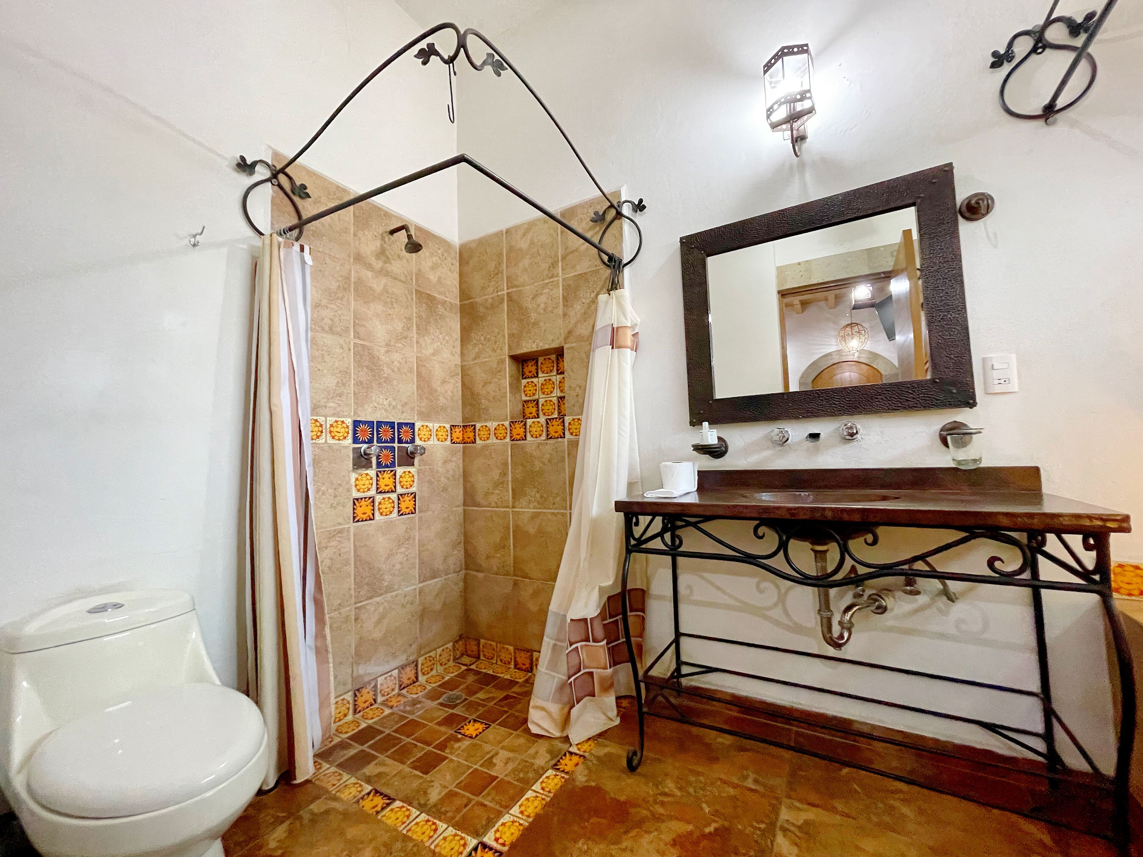 A bathroom with a shower, a toilet, a sink with a mirror, and decorative tiles.