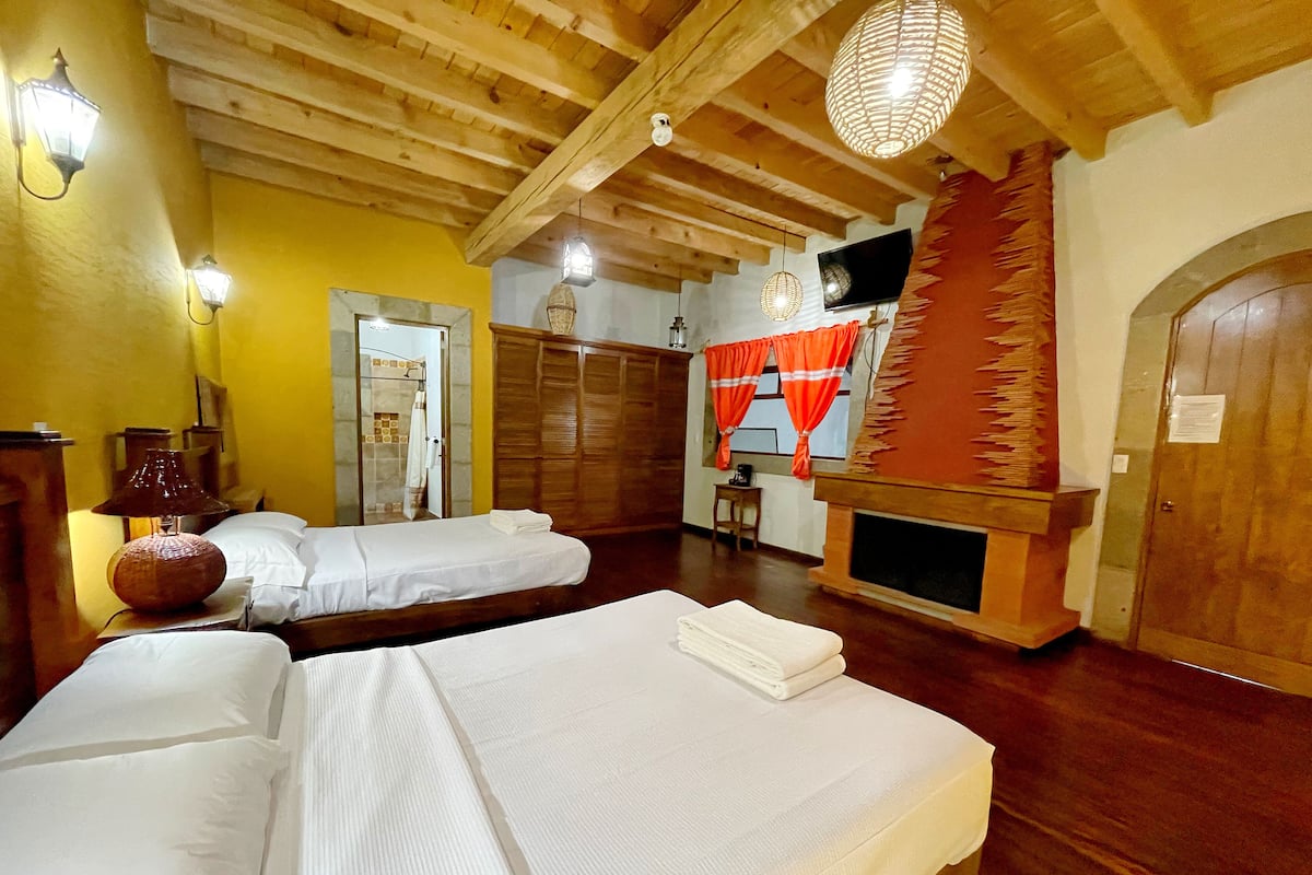 A room with two beds, wooden ceiling beams, a fireplace, and a television.