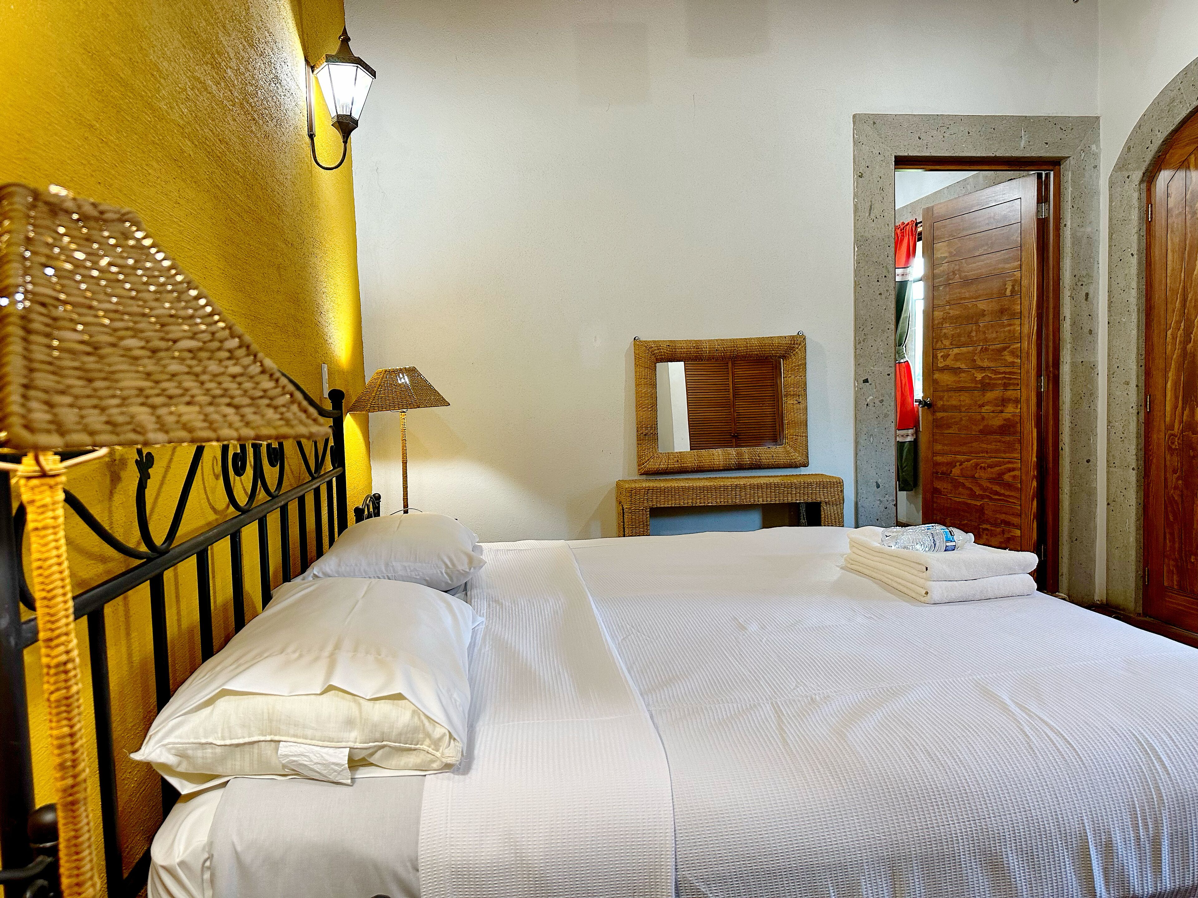 A neatly made bed with white linens, a bedside lamp, and a small wooden nightstand with a mirror.