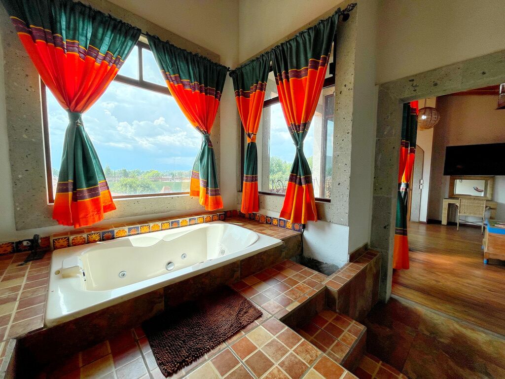 Un baño con bañera, piso de baldosas y cortinas.