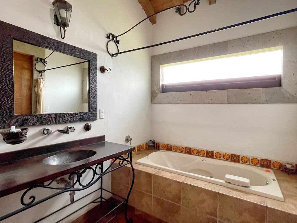 Uma casa de banho com um espelho grande, uma pia, uma banheira e uma janela.