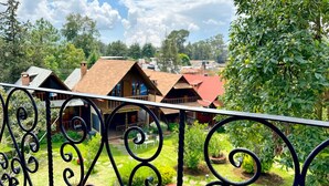 A view of a courtyard with a metal railing, surrounded by greenery and buildings with red roofs. - Sandunga Suites Patzcuaro (Patzcuaro)