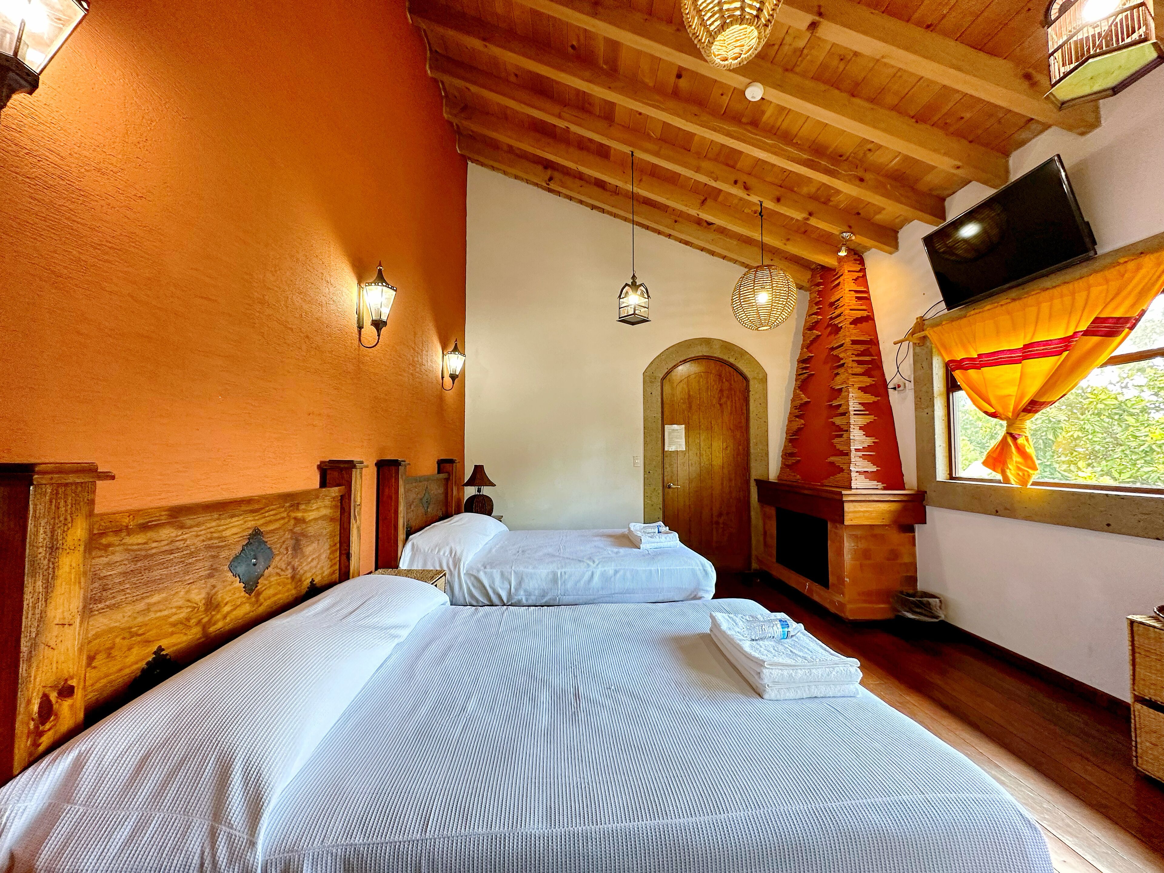 A room with two beds, wooden beams on the ceiling, a fireplace, and a television on the wall.