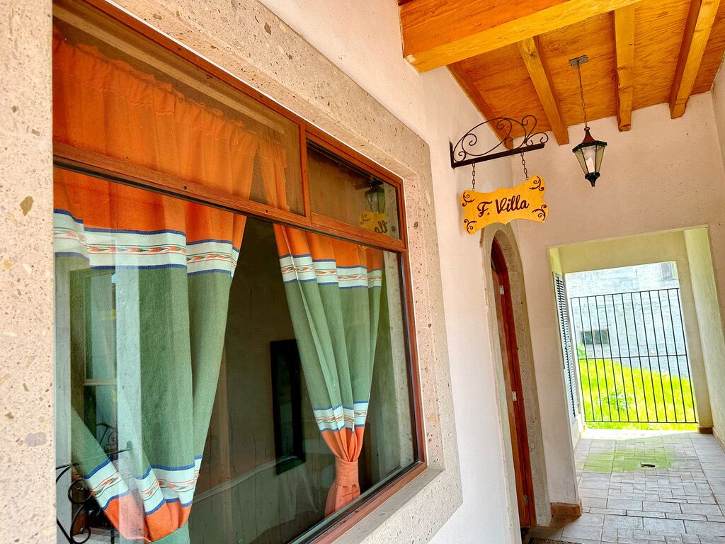 A building entrance with a sign reading "F. Villa," a window with striped curtains, and a wooden ceiling.