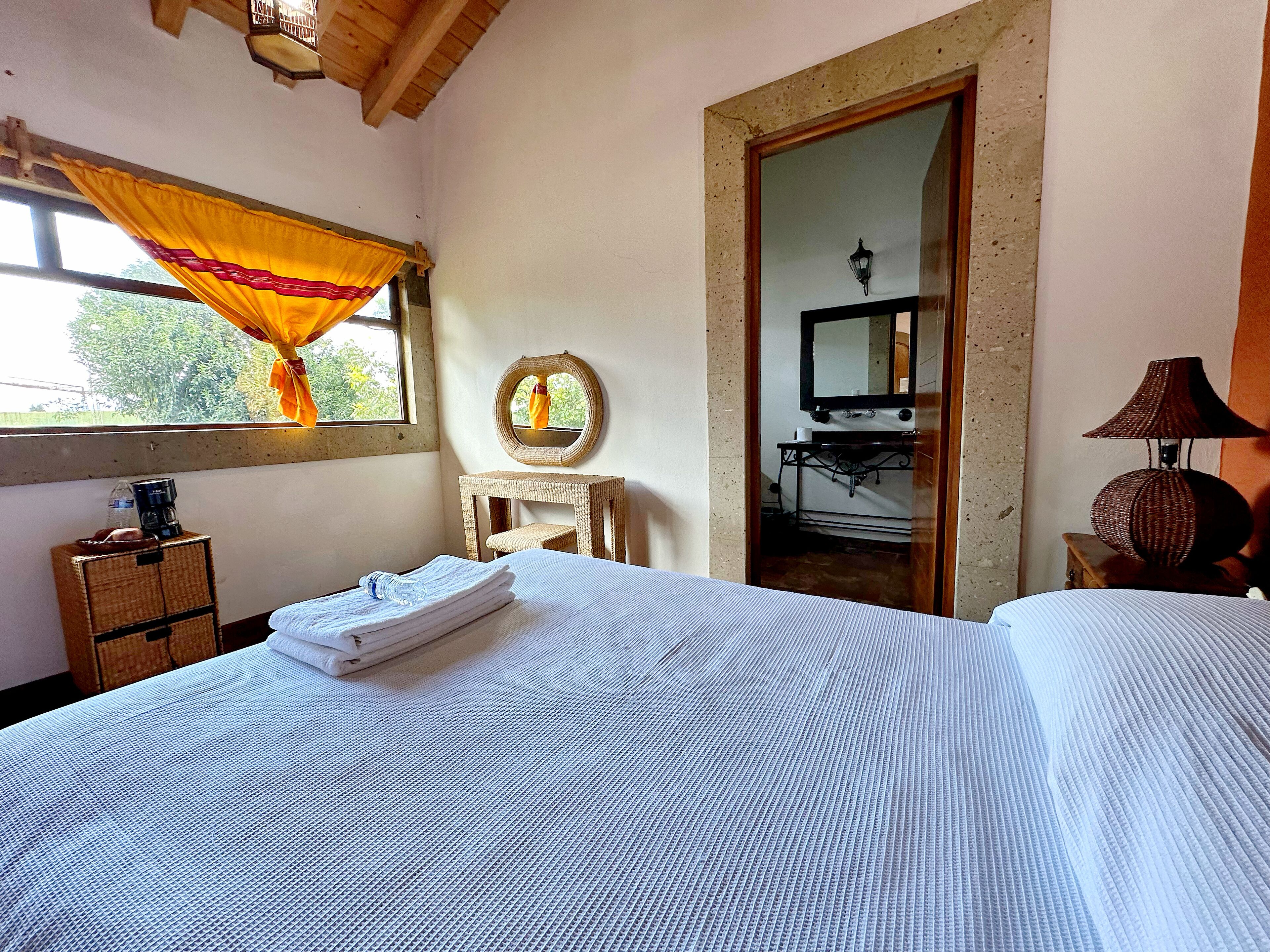 A bedroom with a bed, a small table, a mirror, and a window with curtains.