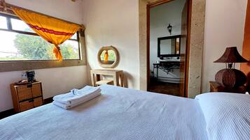 A bedroom with a bed, a small table, a mirror, and a window with curtains.