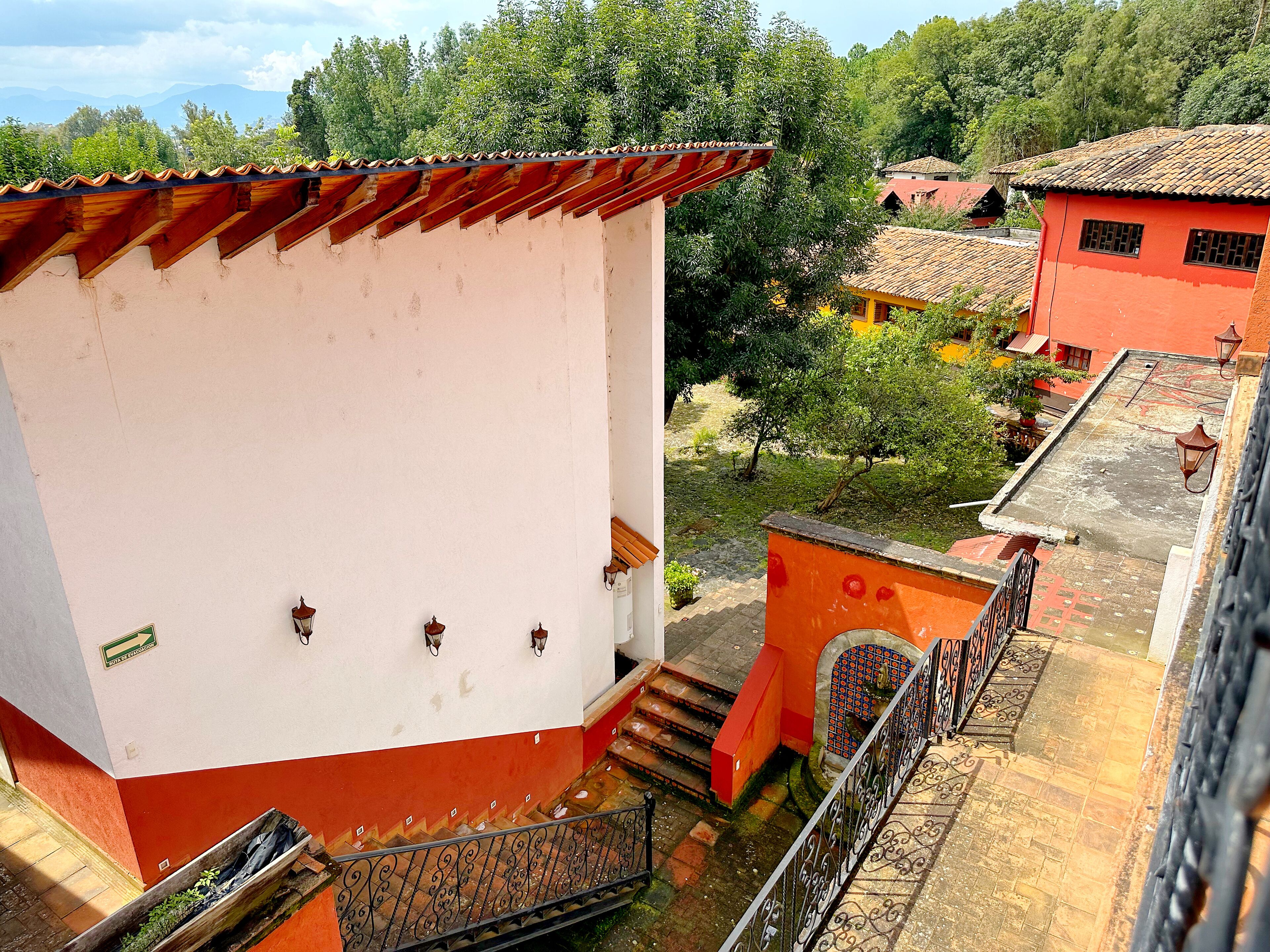 Un immeuble à plusieurs étages, doté d’une façade rouge et blanche, d’un escalier orné de rampes en métal ouvragé, et offrant une vue sur la végétation environnante et les autres bâtiments.
