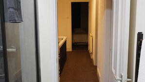 A hallway leading to a bedroom with a bed, a bathroom with a shower, and a door with a towel hanging on it.