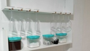 A white shelf with jars and hanging wine glasses. - Apar Aconchegante no Centro de Curitiba  (Curitiba)