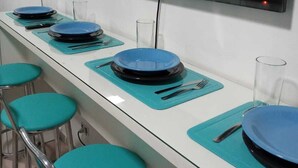 A long dining table with blue plates and cutlery, teal chairs, and a flat-screen TV mounted above. - Apar Aconchegante no Centro de Curitiba  (Curitiba)