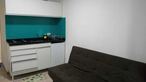 A compact kitchen with white cabinets, a black countertop, and a teal backsplash. - Apar Aconchegante no Centro de Curitiba  (Curitiba)